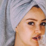 Clean Beauty - Young woman with hair wrapped with towel and bared shoulders drinking water and looking at camera