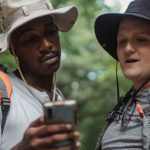 Watch - Young multiethnic hikers with backpacks watching cellphone against trees while spending time together on weekend