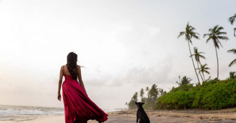 Pet Insurance - A woman in a red dress walking on the beach with a dog