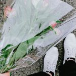Gift - Top view of anonymous person in casual clothes and white sneakers holding bouquet of flowers and standing on asphalt